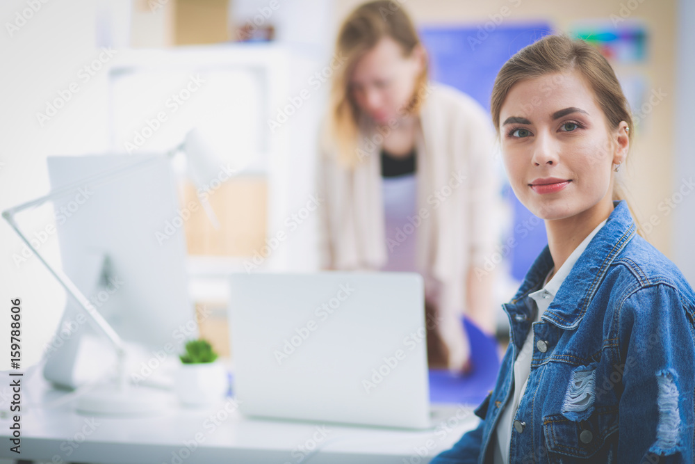 Two young woman sitting near desk with instruments, plan and laptop. Two young woman sitting near desk with instruments, plan and laptop.