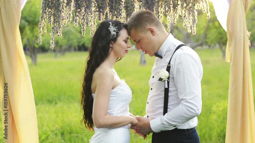 Close-up of a charming couple, man speaking the words of love to his lovely sweetheart. Dark-haired woman and a man with short hair in wedding dresses. Close-up of a charming couple, man speaking the words of love to his lovely sweetheart. Dark-haired woman and a man with short hair in wedding dresses.