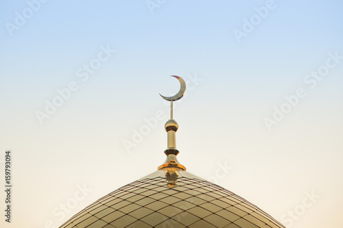 The top of the golden minaret with a golden crescent on the background of sunset or sunrise. In the center of the frame.