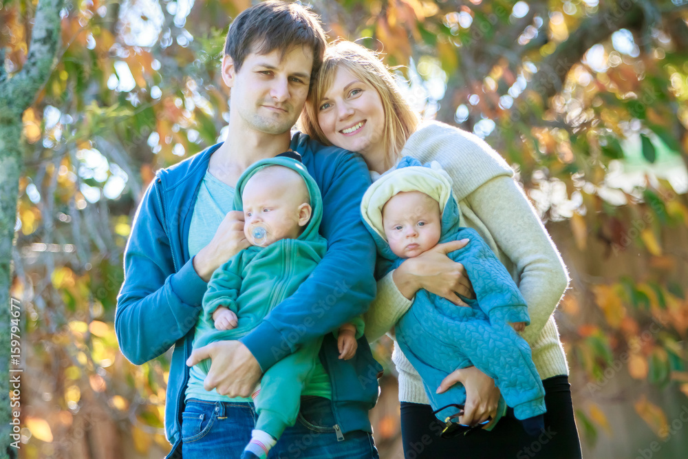outdoor portrait of young happy smiling mother and father with twin babies on natural background outdoor portrait of young happy smiling mother and father with twin babies on natural background