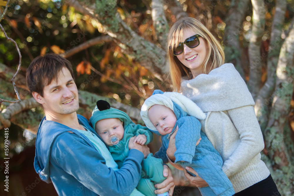 Naklejka premium outdoor portrait of young happy smiling mother and father with twin babies on natural background