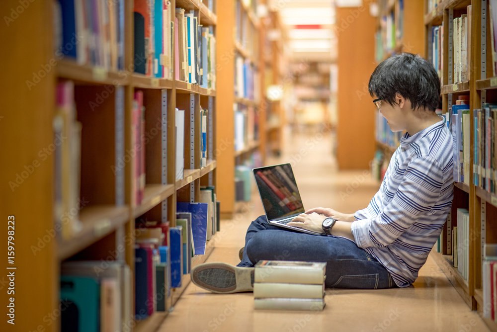 Young Asian man university student thinking about his project homework and using laptop computer in library, education research and self learning in university life concepts Young Asian man university student thinking about his project homework and using laptop computer in library, education research and self learning in university life concepts