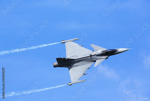 Modern jet fighter flying against a blue sky. White smoke trail. photo