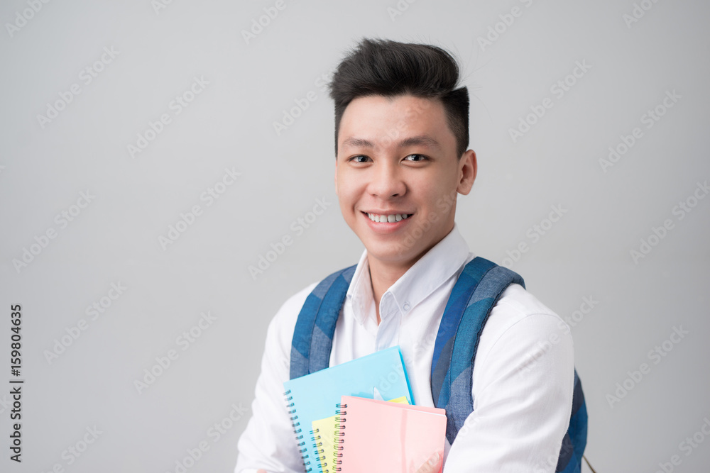Happy casual asian male student holding books isolated on a gray background Happy casual asian male student holding books isolated on a gray background