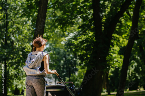 Young mother jogging with a baby buggy in summer park