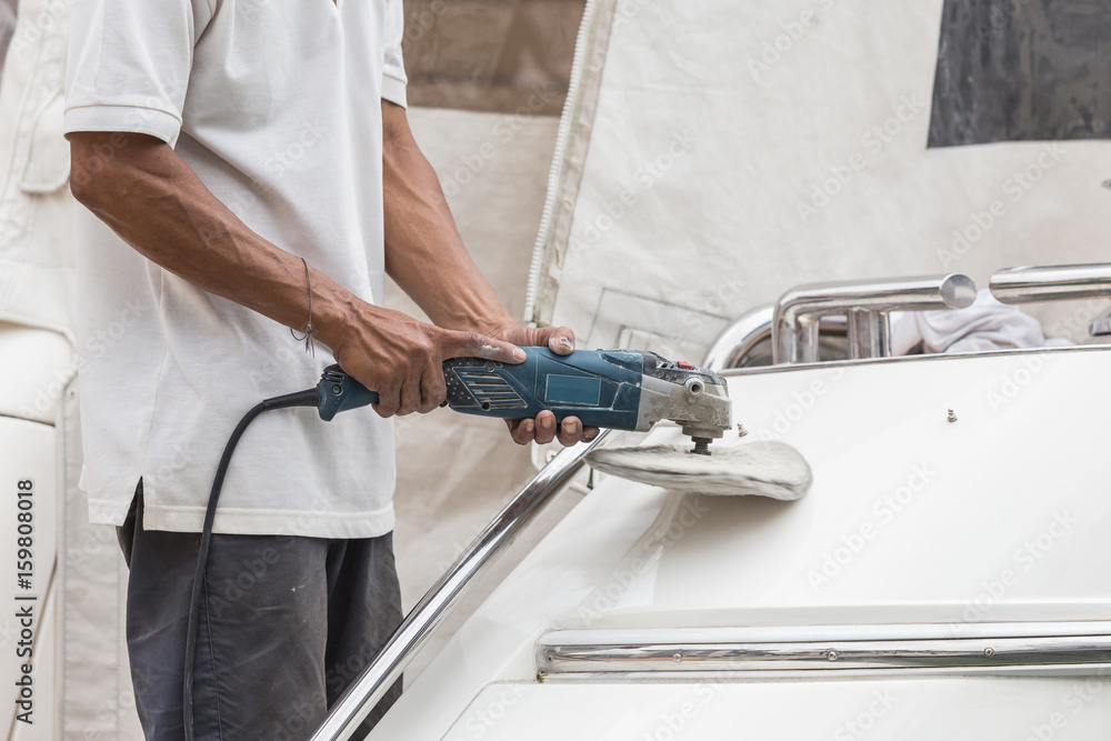 Yacht maintenance. A man polishing side of the white boat in the marina Yacht maintenance. A man polishing side of the white boat in the marina