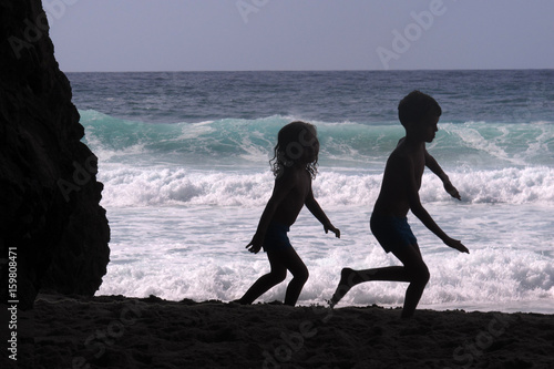 Silhouette of two children play near a rock formation near the sea near Csacais, Portugal