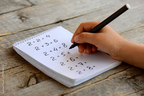 Child solves mathematics examples. Child holds a black marker in his hand. Notebook sheet with multiplication table examples. Studying a multiplication table concept