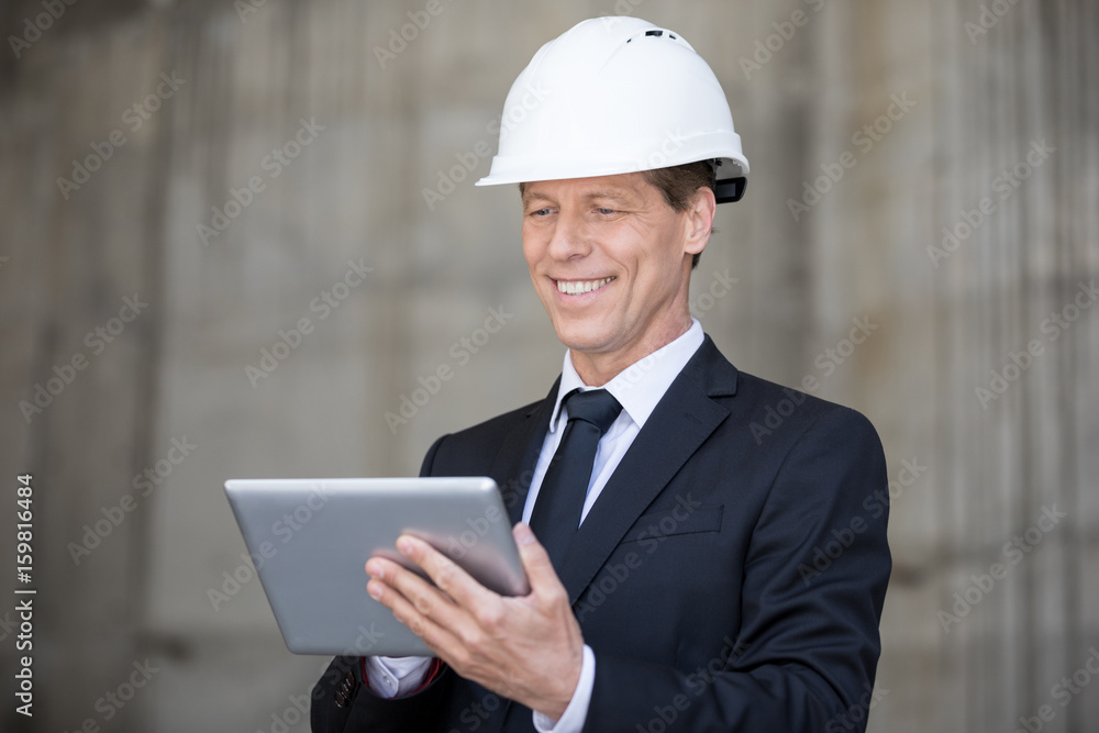 Smiling middle aged businessman in hard hat using digital tablet Smiling middle aged businessman in hard hat using digital tablet