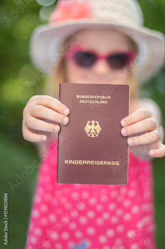 Sommerlich gekleidetes Mädchen hält Kinderreisepass in den Händen