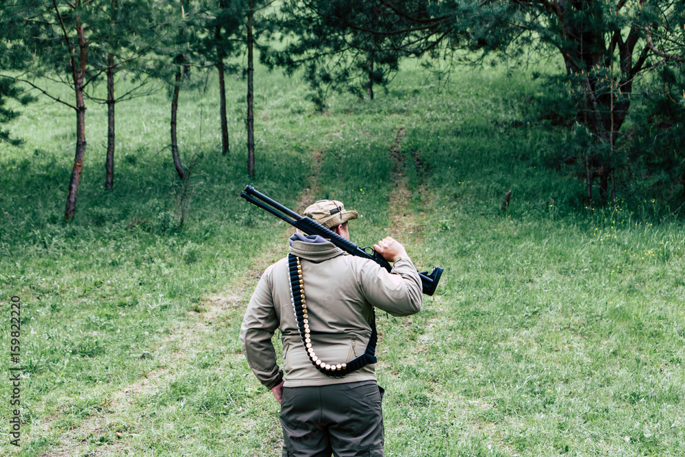 Fototapeta premium Hunter with a gun. Standing in the forest and waiting for prey