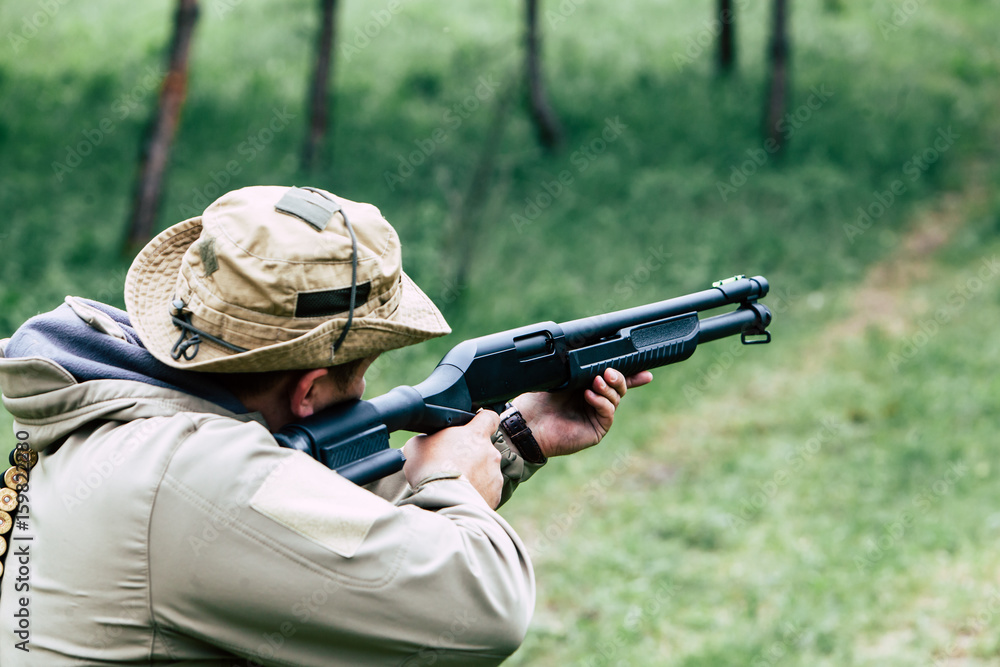 Fototapeta premium Hunter with a gun. Standing in the forest and waiting for prey