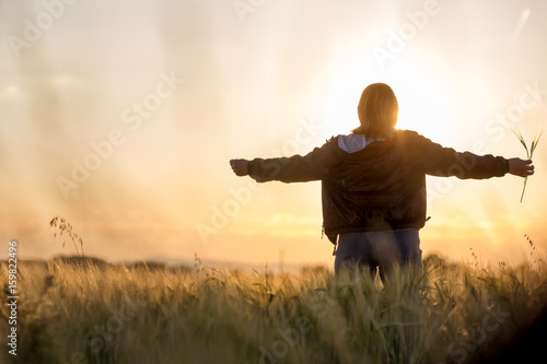Middle aged caucasian woman standing in the sunlit field with open arms, embracing nature