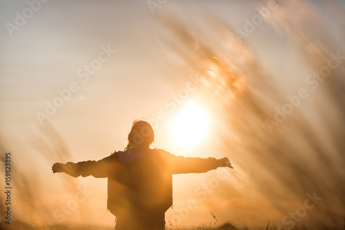 Middle aged caucasian woman standing in the sunlit field with open arms, embracing nature