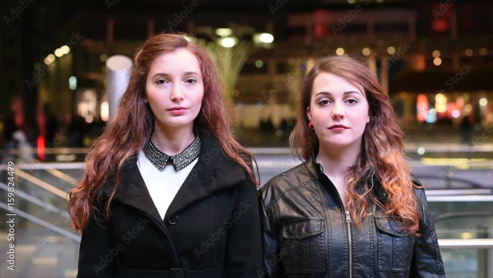 Waist up of two young beautiful caucasian women friends outdoor in the city night posing looking over, hand in hand serious - pensive, thoughtful concept Waist up of two young beautiful caucasian women friends outdoor in the city night posing looking over, hand in hand serious - pensive, thoughtful concept