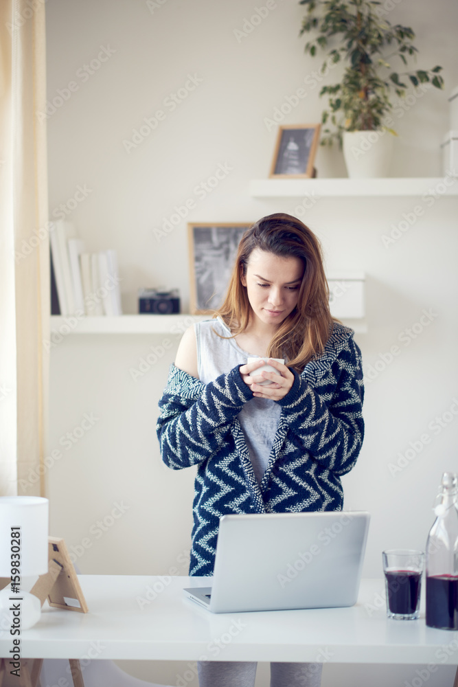 Beautiful Caucasian girl standing in living room and using laptop in the morning Beautiful Caucasian girl standing in living room and using laptop in the morning
