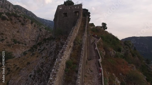 Climb Ancient Fortress ctone wall Kotor above old town on the high mountain Montenegro. Europe UNESCO list famous tourist attraction. Aerial drone flight close.  photo