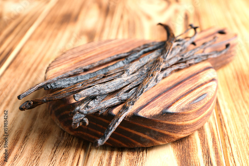 Board with dried vanilla sticks on wooden table, closeup