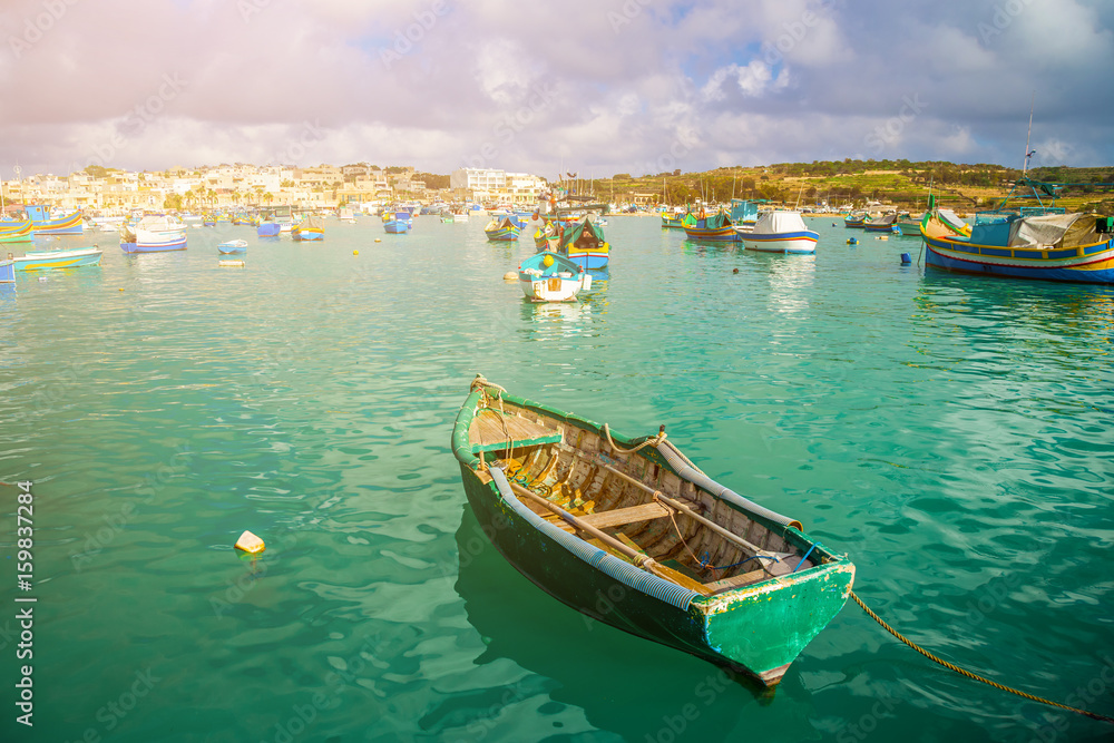 Marsaxlokk, Malta - Traditional green maltese Luzzu fisherboat at the old market of Marsaxlokk with green sea water, blue sky and palm trees on a summer day
