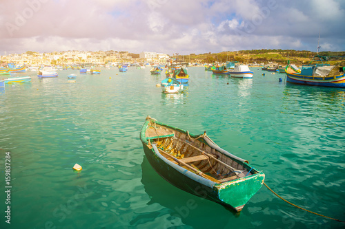 Marsaxlokk  Malta - Traditional green maltese Luzzu fisherboat at the old market of Marsaxlokk with green sea water  blue sky and palm trees on a summer day