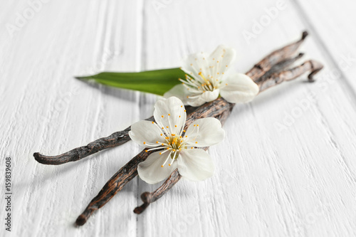 Dried vanilla sticks and flowers on light wooden background, closeup