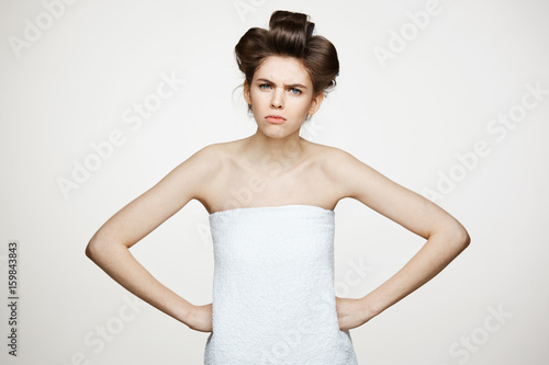 Portrait of young displeased girl in hair curlers looking at camera over white background. Beauty cosmetology and spa.