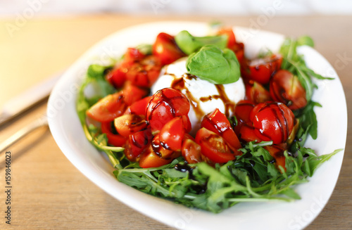 tomato mozzarella salad served in a white plate with oil, balsamic and basil leaves