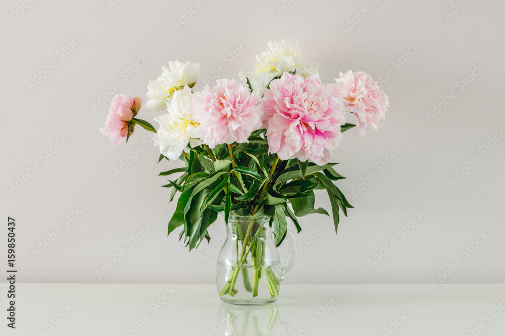 Bouquet of white and pink peonies in glass vase on white background