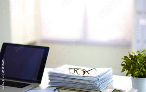 Laptop with stack of folders on table on white background © lenetsnikolai
