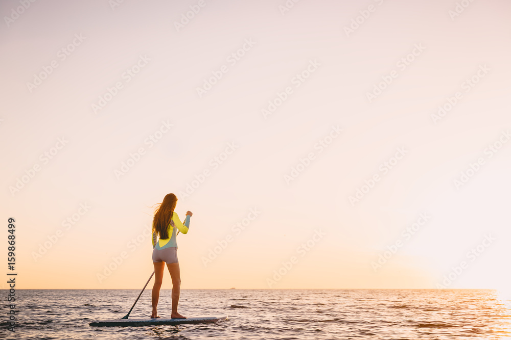 Sporty woman in ocean on stand up paddle surfboard and beautiful sunset colors