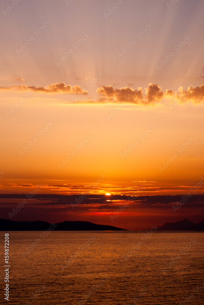 panoramic image of golden sunset with sun low above the sea and sunrays coming through clouds above