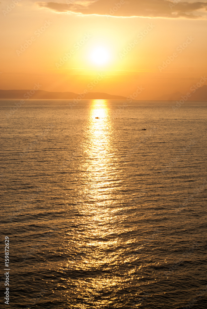 golden sunset over the sea with sun high in the sky and a boat in the beam of light 
