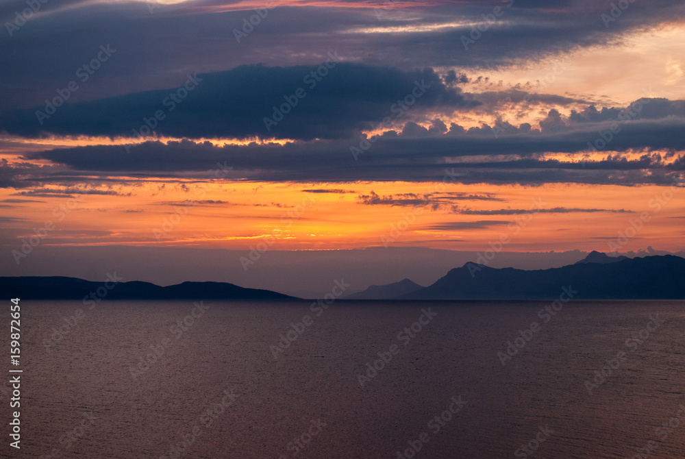 Horizontal image of deep coloured sunset with blue, purple and golden hues, black mountains on the horizon,