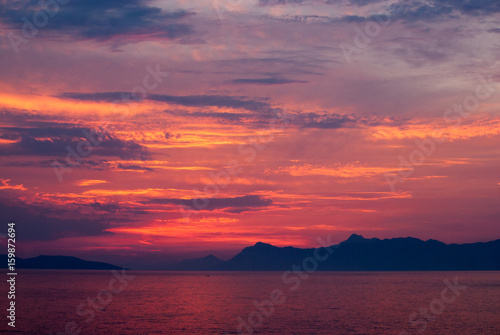 Horizontal image of deep coloured sunset with sea in red  golden and purple colours  black mountains on the horizon 