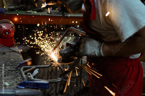 Worker using an electric grinder on steel structure in a workshop with sparks flying in the air.