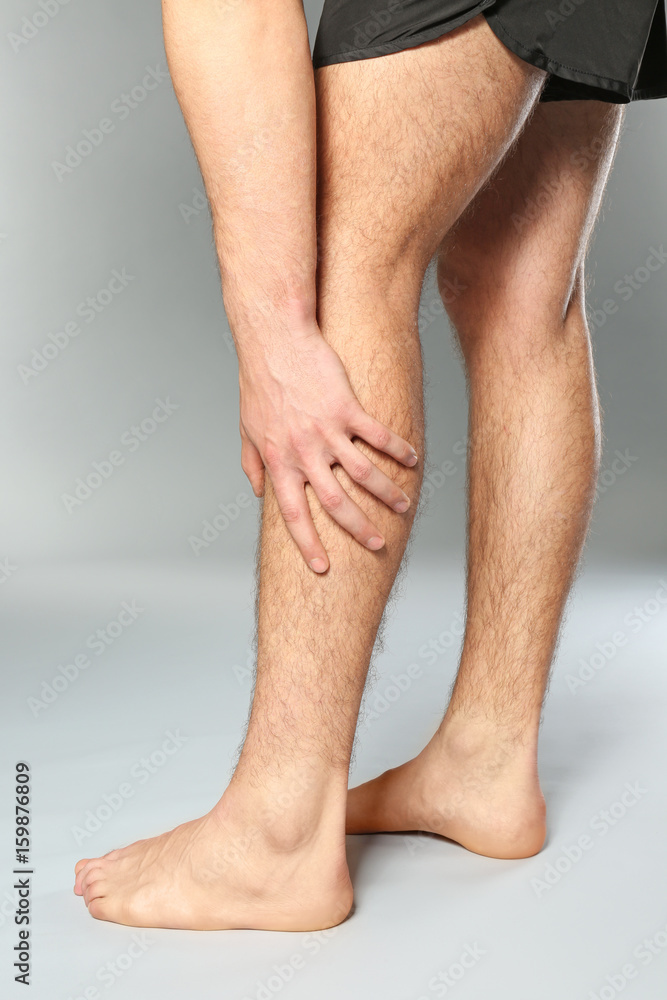 Young man suffering from pain in leg on grey background