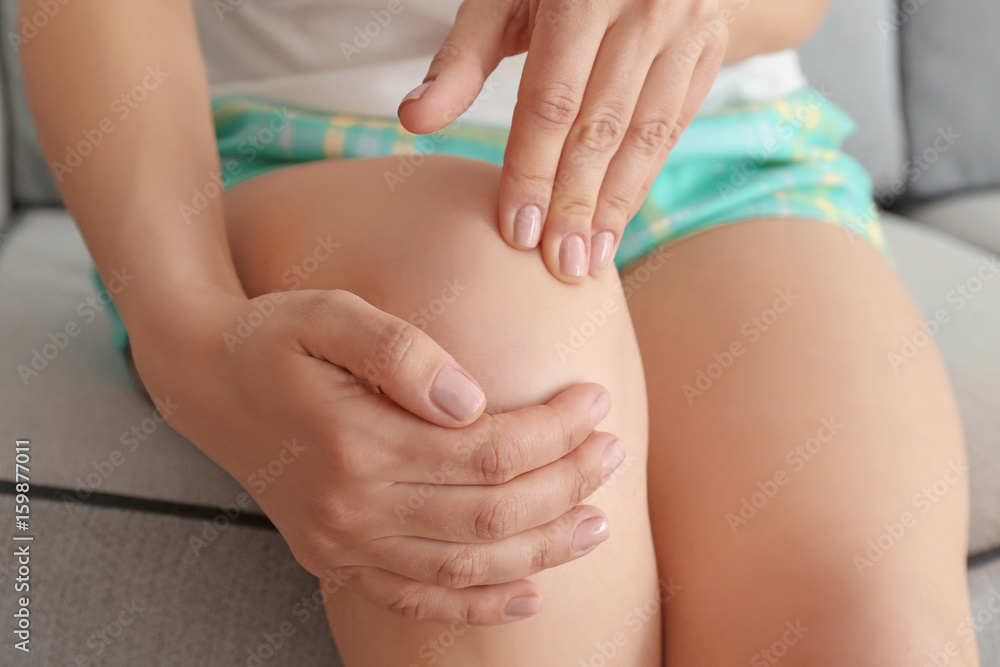 Fototapeta premium Young woman suffering from pain in leg at home, closeup