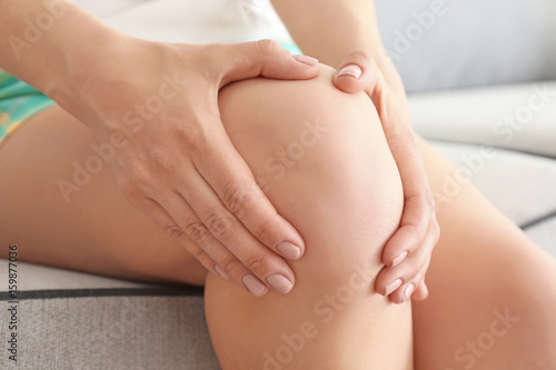 Young woman suffering from pain in leg at home, closeup