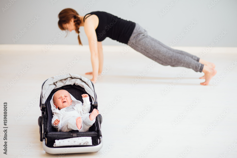 Cute little boy crying in baby carrying while his mother doing
