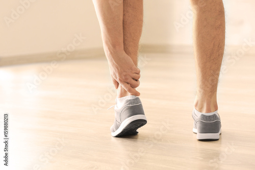 Young man suffering from pain in leg indoors