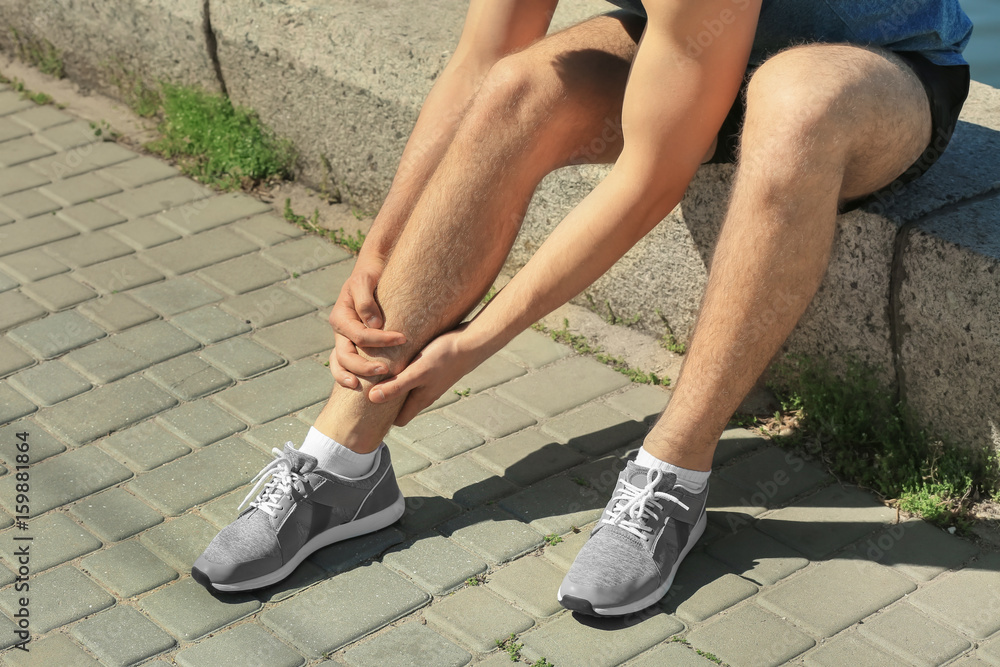 Young man suffering from pain in leg outdoors Young man suffering from pain in leg outdoors