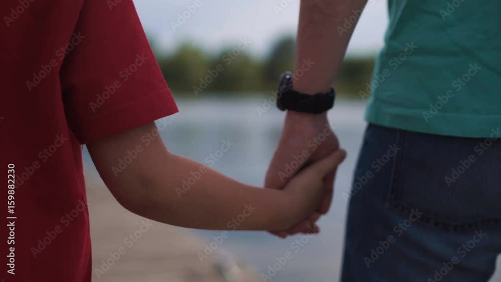 Anonymous father holding hand of son while walking. Anonymous father holding hand of son while walking.