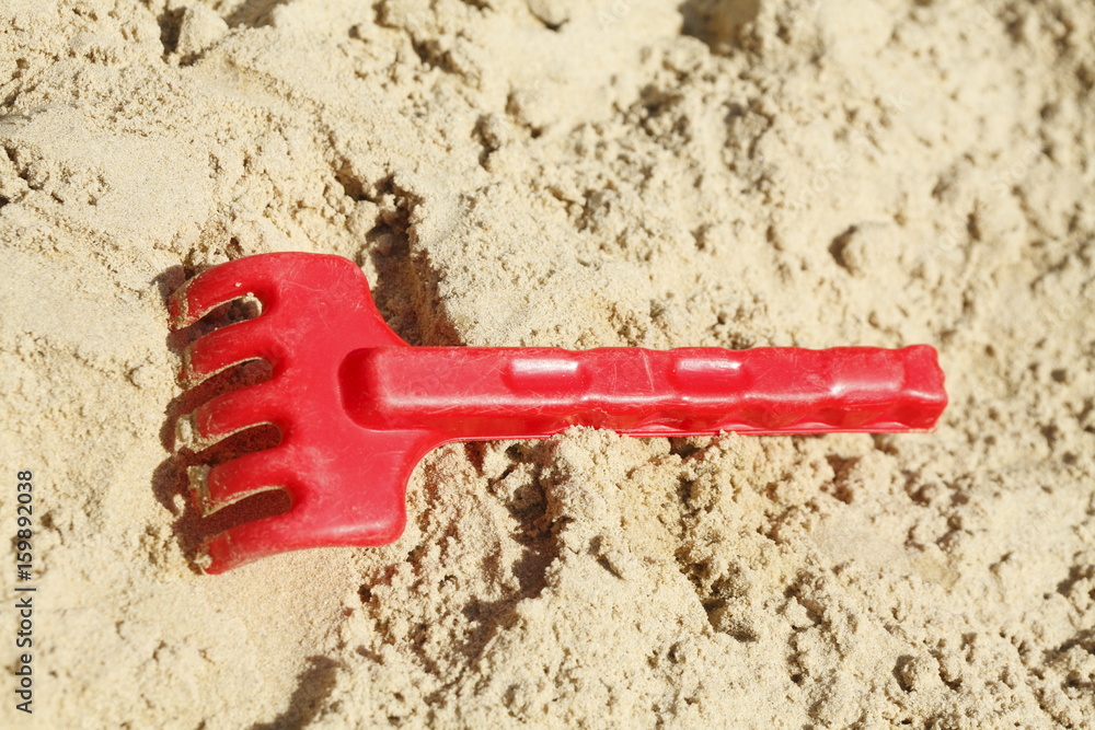 Harke, Plastikspielzeug in einem Sandkasten Harke, Plastikspielzeug in einem Sandkasten