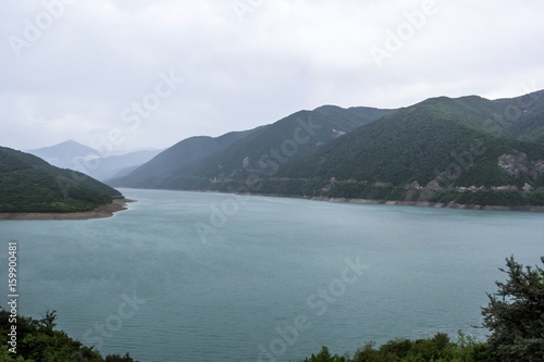 Живописное озеро в горах, водоем в горном ущелье между зеленых холмов, пасмурная погода, отдых на природе