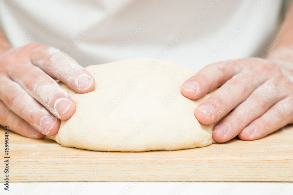Chef's hands kneading the dough on the wooden board. Preparation for baking.