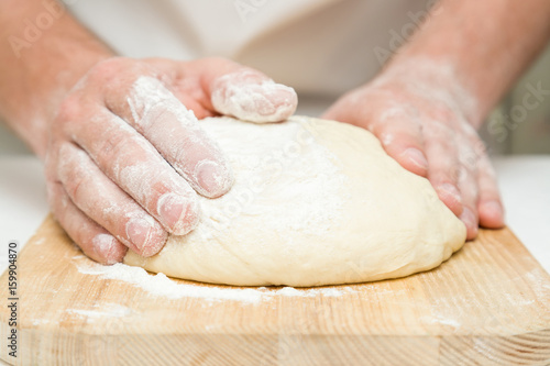 Chef's hands kneading the dough on the wooden board. Preparation for baking.