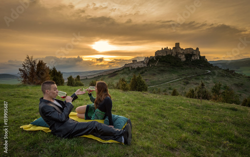 Couple drink red wine in nature under the ruins of a castle at sunset.