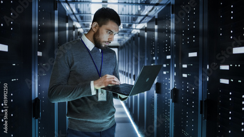 Fotografia IT Technician Works on a Laptop in Big Data Center full of Rack Servers