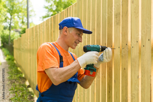 Handyman twirls a screw into the wooden fence wearily smiling