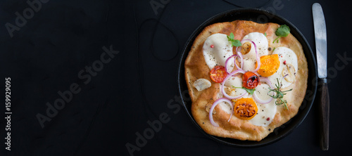 Small homemade pizza with mozzarella cheese, tomatoes, herbs on rustic wooden table. Top view. Copy space. Wide panoramic image. Copy space.